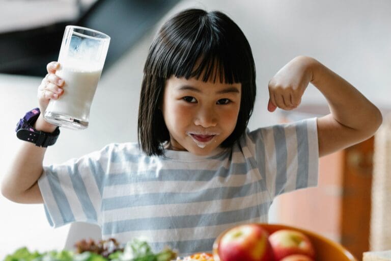 Child drinking milk and smiling during healthy snack time in a play based childcare early learning environment.