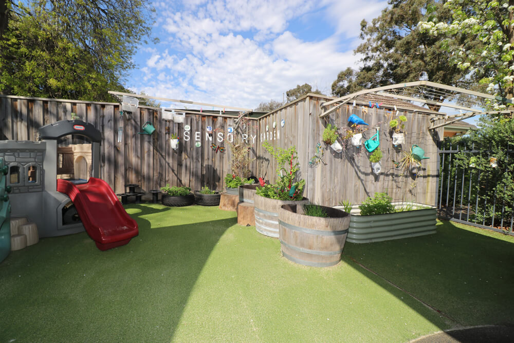 Childcare sensory garden with plants, raised garden beds and outdoor play equipment supporting nature based early learning.