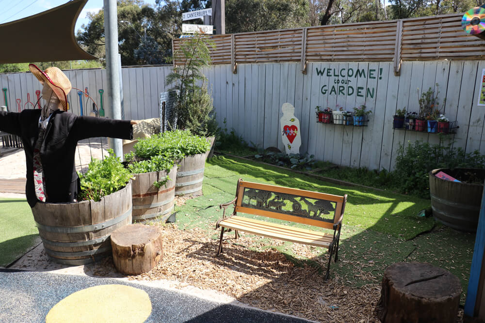 Childcare kitchen garden area with planter boxes, bench seating and scarecrow supporting outdoor early learning.