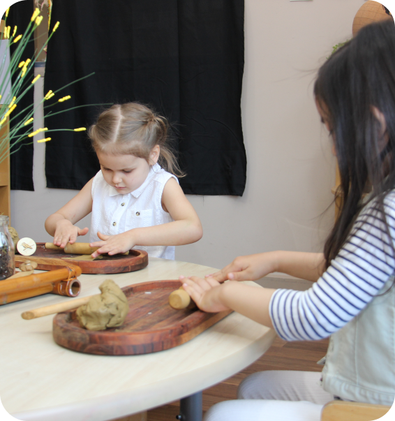 Two young children shaping playdough with wooden tools at a round table in a safe, age-appropriate classroom