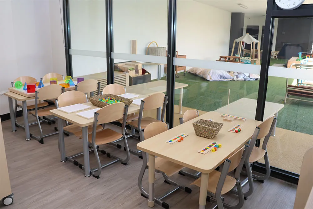 Childcare classroom learning tables with activity materials and view to outdoor early learning play area.