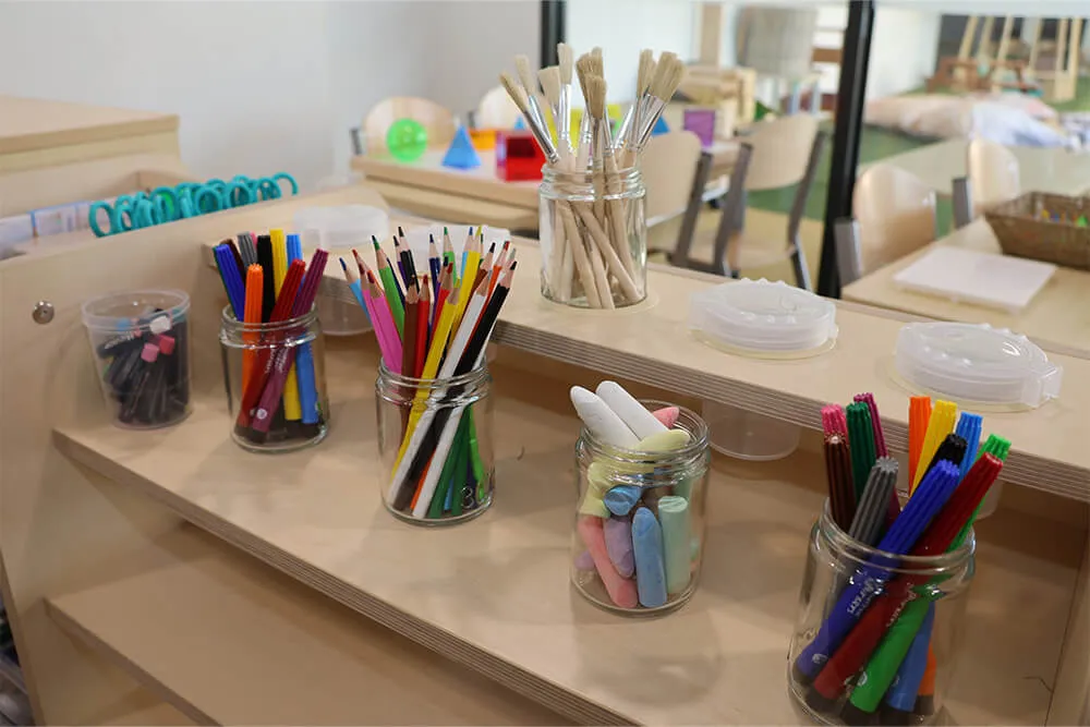 Childcare art station with jars of coloured pencils, chalk and brushes supporting creative early learning.