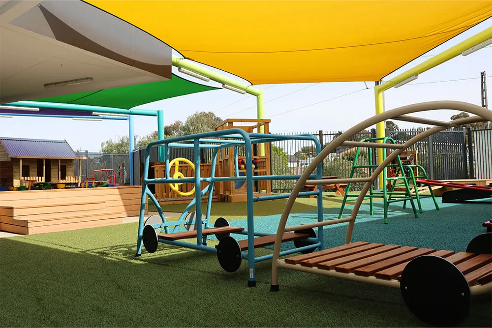 Shaded outdoor childcare playground with climbing frames, balance bridges and active play equipment.