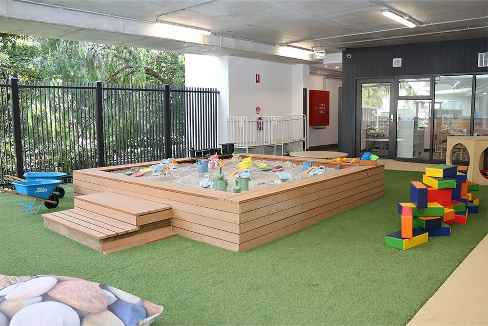 Outdoor childcare sandpit play area with toys and building blocks supporting hands-on early learning.