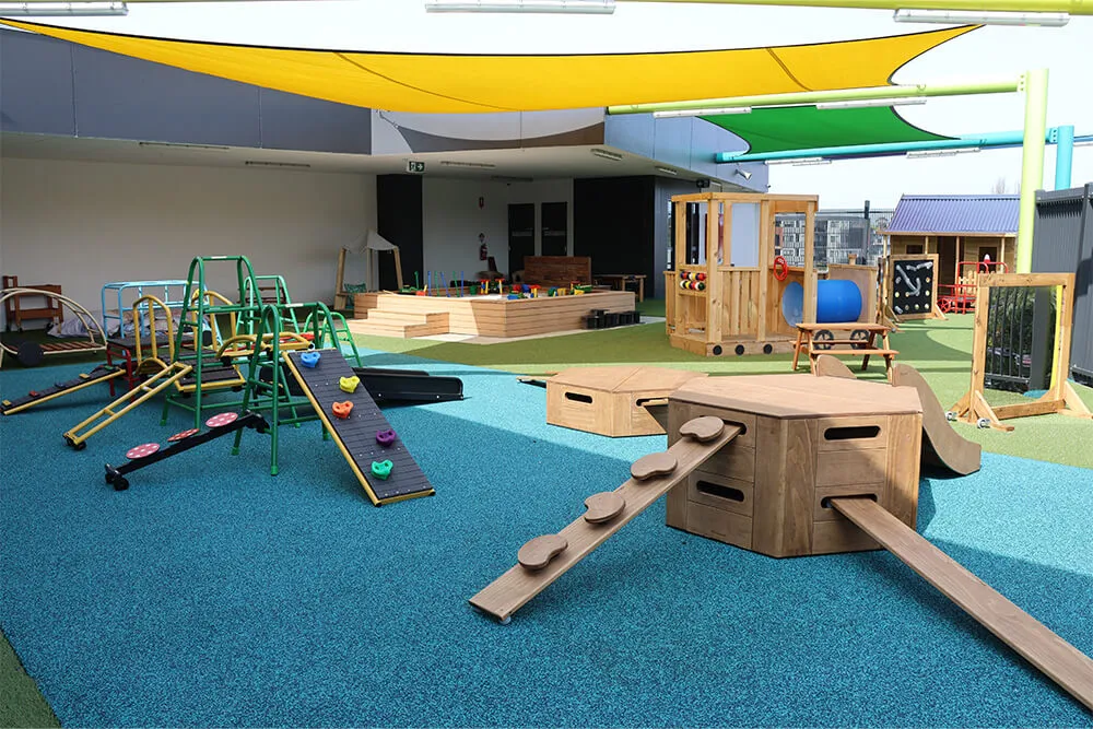 Large outdoor childcare playground with climbing ramps, balance beams and shaded play areas for active early learning.