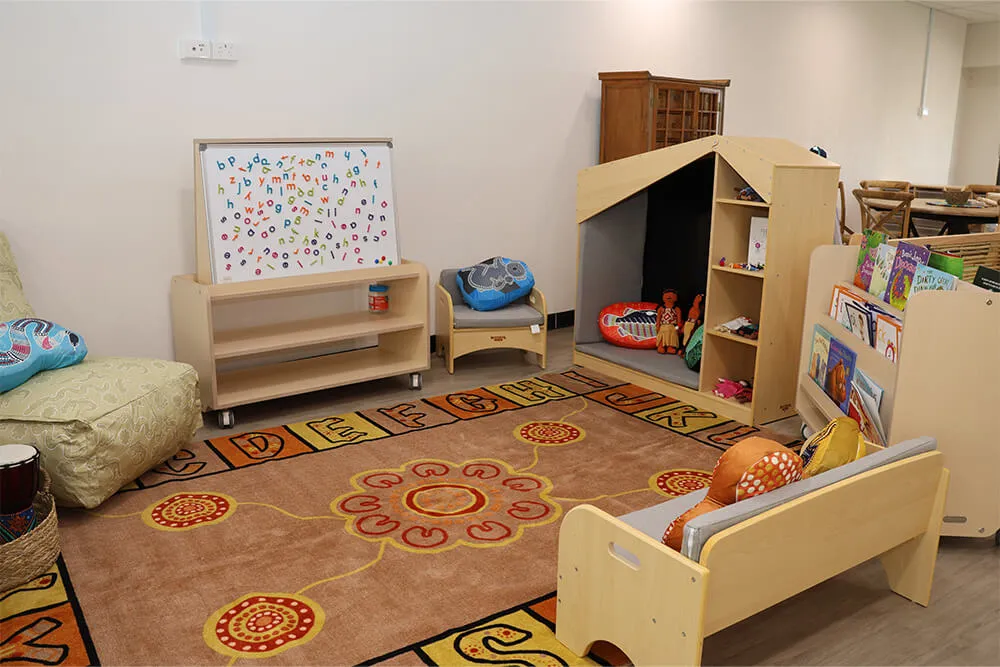 Childcare quiet learning corner with alphabet rug, books, playhouse and soft seating for early learning.