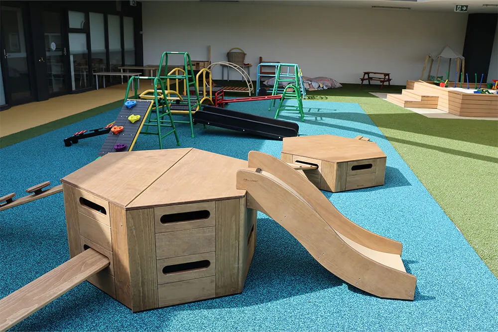 Outdoor childcare playground with wooden climbing platforms, slides and balance equipment for active early learning.