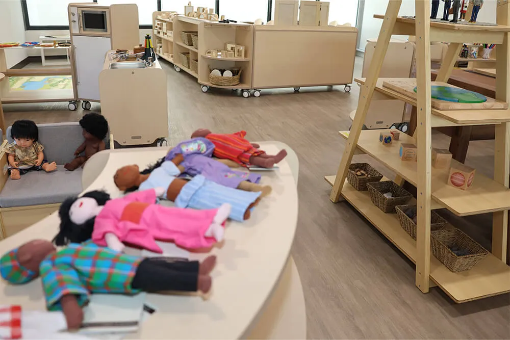 Childcare dramatic play area with dolls, shelves and learning materials supporting imaginative early learning.