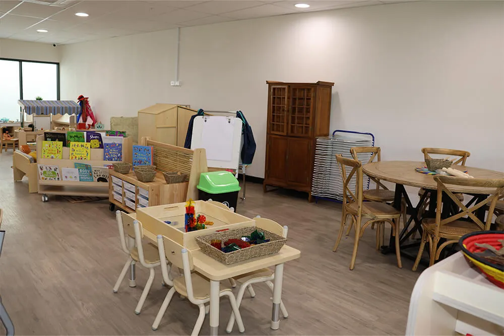 Childcare classroom with learning tables, books and play materials supporting early learning and kindergarten activities.
