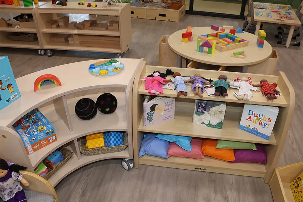 Childcare learning shelves with books, dolls, blocks and play materials supporting early learning and imaginative play.