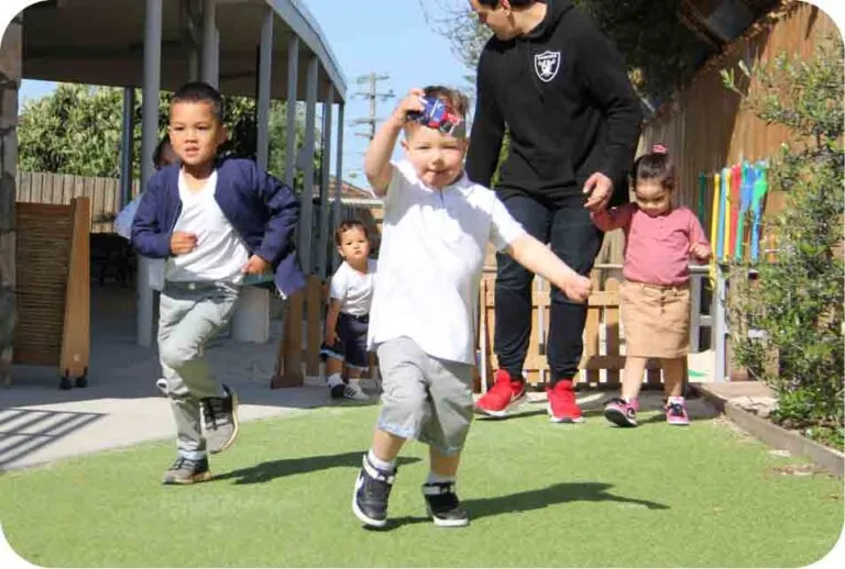 Children running and playing outdoors with an educator during active play at a childcare early learning centre.