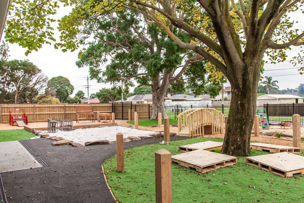 Outdoor childcare playground with sandpit, wooden bridge and natural play areas supporting safe early learning and exploration.