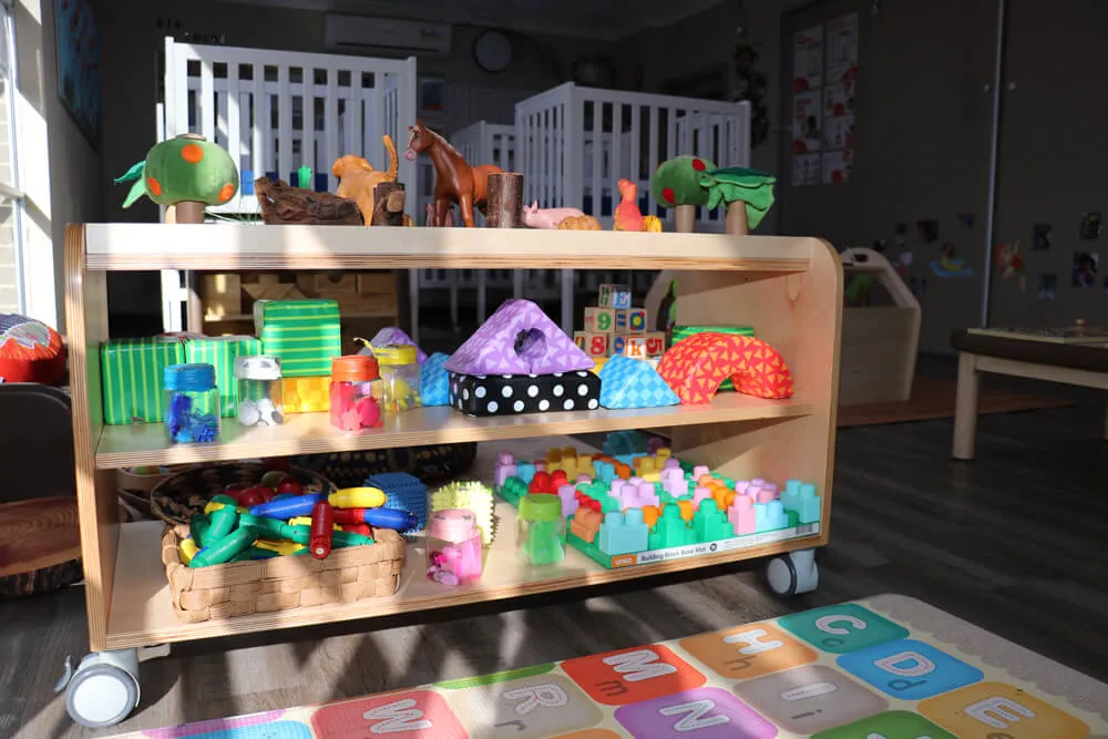 Childcare learning shelf with toys, sensory materials and play resources in a bright early learning classroom.