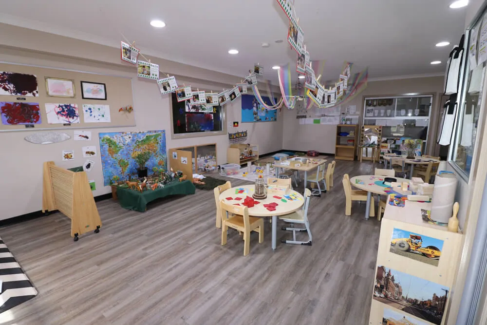 Spacious kindergarten classroom with activity tables, learning displays and creative play areas in an early learning childcare centre.