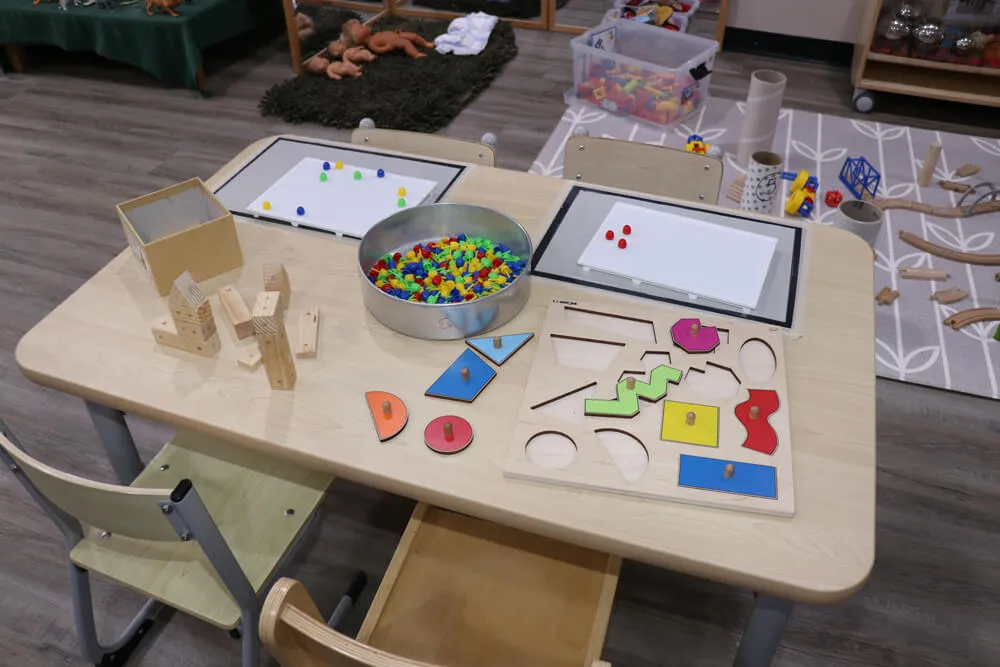Early learning activity table with puzzles, counting beads and wooden blocks supporting play based childcare.