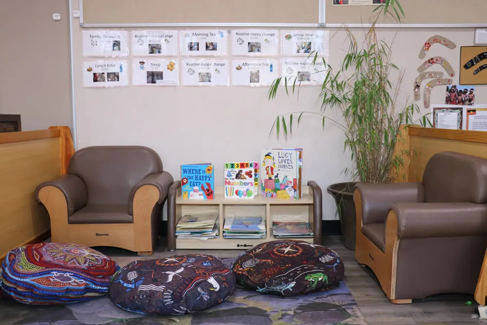 Calm reading corner with books, soft cushions and chairs in a kindergarten early learning classroom.