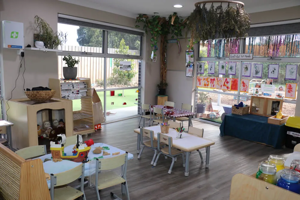 Bright early learning classroom with natural materials, artwork displays and small tables in a Reggio Emilia inspired childcare space.