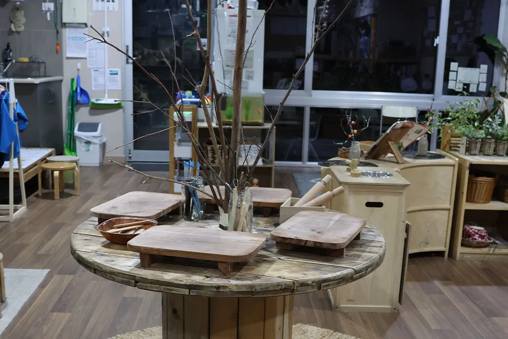 Nature-inspired early learning table with branches, wooden trays and sensory materials in a childcare classroom.