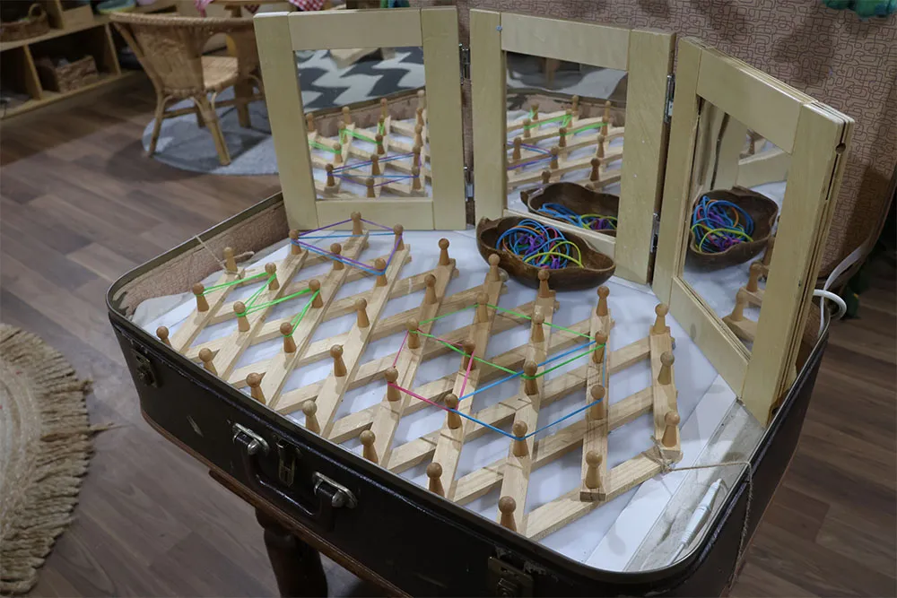 Child using wooden peg board with rubber bands and mirrors for hands-on early learning in a childcare classroom.