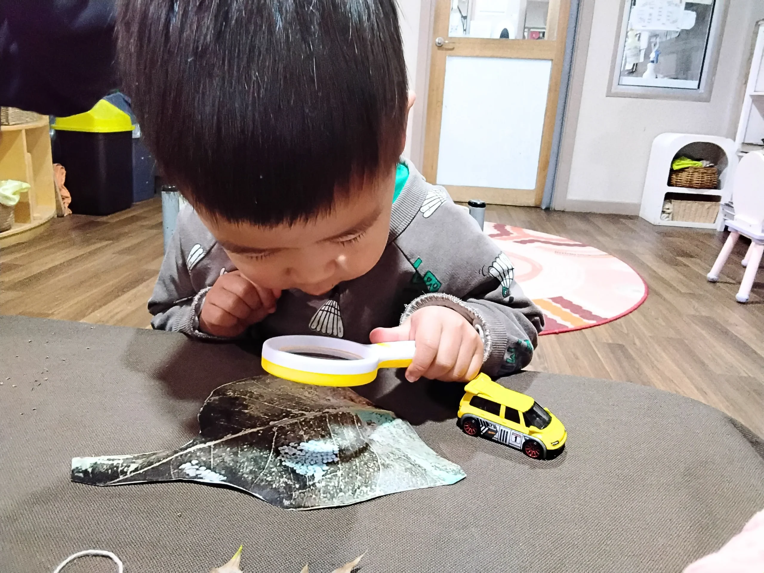 Child using a magnifying glass during a hands-on learning activity at Starfish ELC