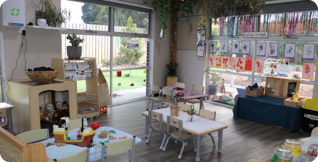 Bright early learning classroom with natural materials, artwork displays and small tables in a Reggio Emilia inspired childcare space.