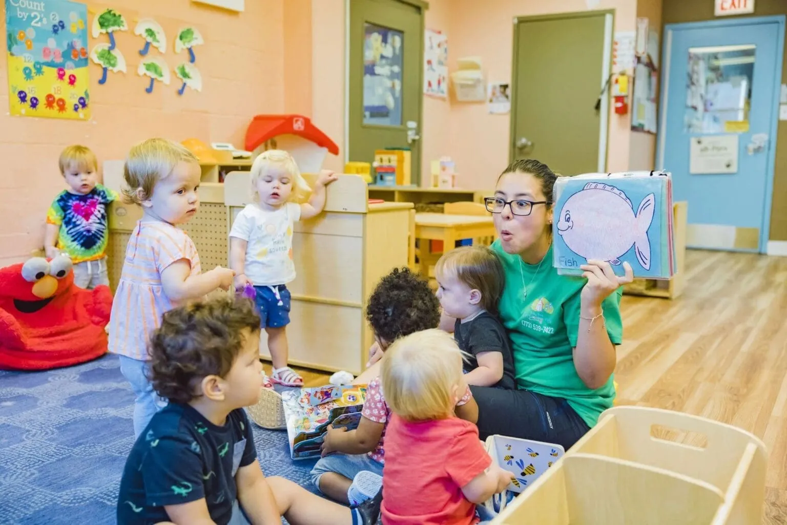 Educator reading a picture book to toddlers during a group early learning activity in a childcare classroom.