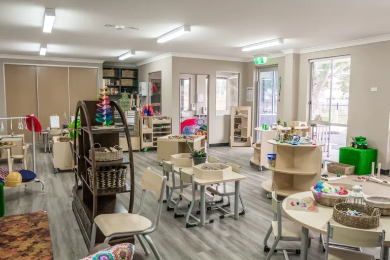 Spacious childcare classroom with play based learning stations, tables and educational resources supporting early learning.