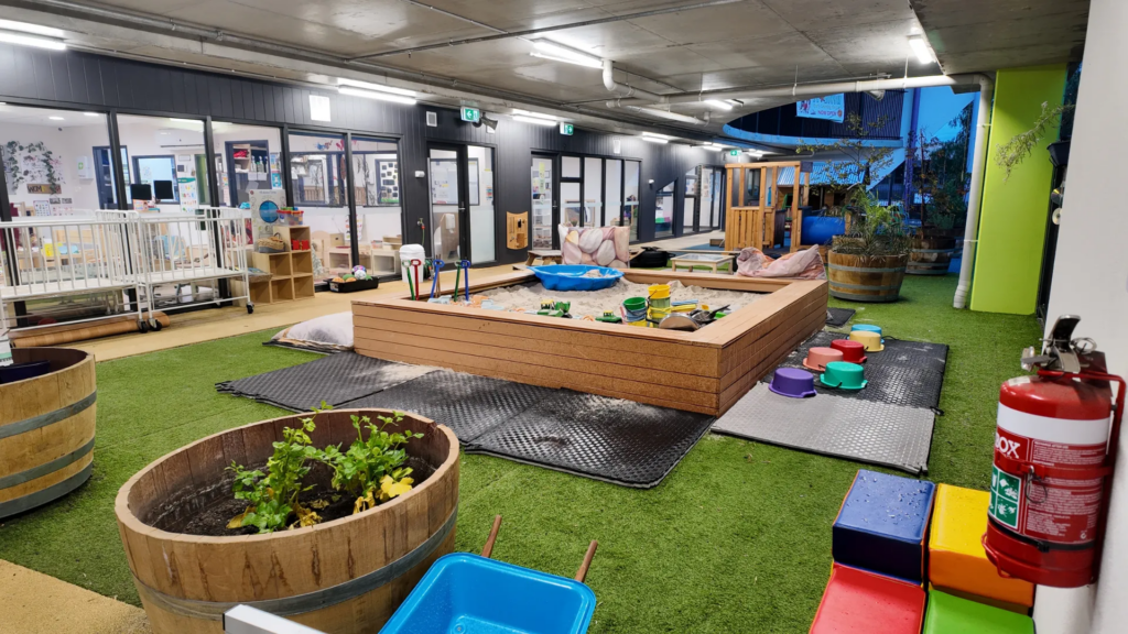 Questions to ask childcare centre when touring, with a view of an indoor-outdoor play area featuring activity spaces, toys, seating and garden planters.